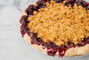 Dark berry filling spills out of an open face pie with crumble topping