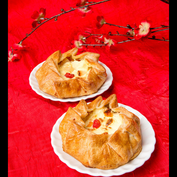 Two custard galettes topped with fruit cocktail on white plates. Background: A red tablecloth with cherry blossoms.